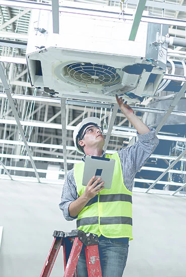 HVAC professional inspecting a ceiling-mounted ventilation and air conditioning unit
